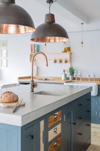 A modern kitchen featuring cool blue cabinetry paired with elegant copper fixtures, creating a stylish and contemporary look. The copper accents include handles and lighting, adding warmth to the cool tones.