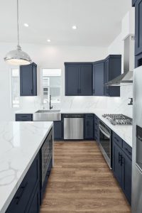 A sophisticated kitchen featuring deep marine blue cabinets, exuding elegance and style. The cabinets are paired with gold hardware and luxurious marble countertops, creating a high-end look.